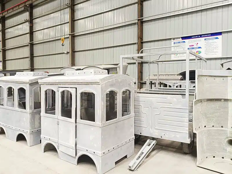 Multiple unfinished train carriages in the factory, designed for electric trackless train rides, awaiting final assembly.