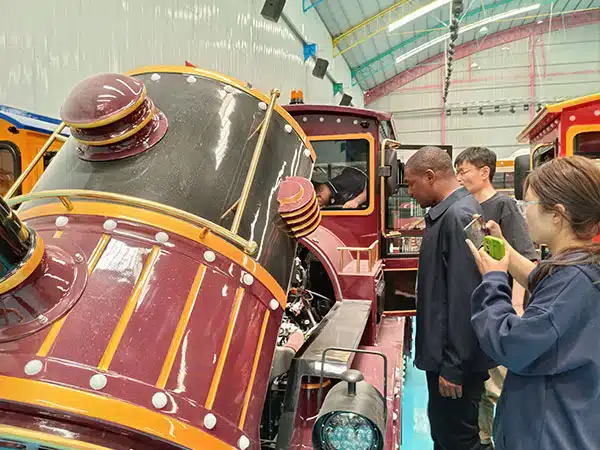 Customers checking the structure and details of a trackless train inside Carnee Rides factory