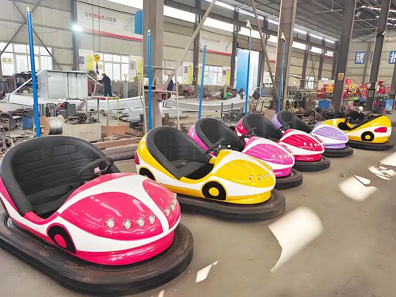 Factory setup for ceiling bumper cars in production, showcasing various models such as pink, yellow, and purple bumper cars ready for installation. Designed for amusement parks with customizable designs and vibrant lights.