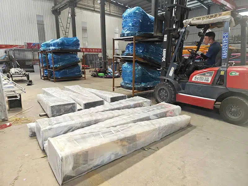Factory workers packing bumper car floor grid panels and wrapped units, with a forklift preparing items for shipment.