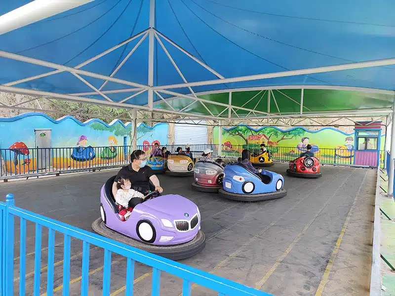 Families riding ground grid bumper cars in an indoor amusement park, featuring safe 2-seat electric floor-grid bumper cars for all ages.