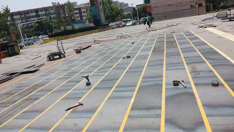 Outdoor ground grid bumper car floor installation with conductive steel plates and copper strips being laid on site.