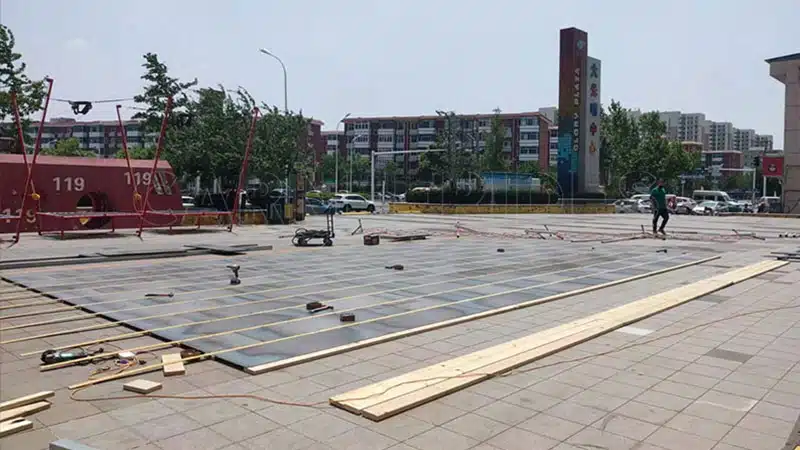 Outdoor installation of floor grid bumper car track, showing conductive rails and steel floor panels in progress.