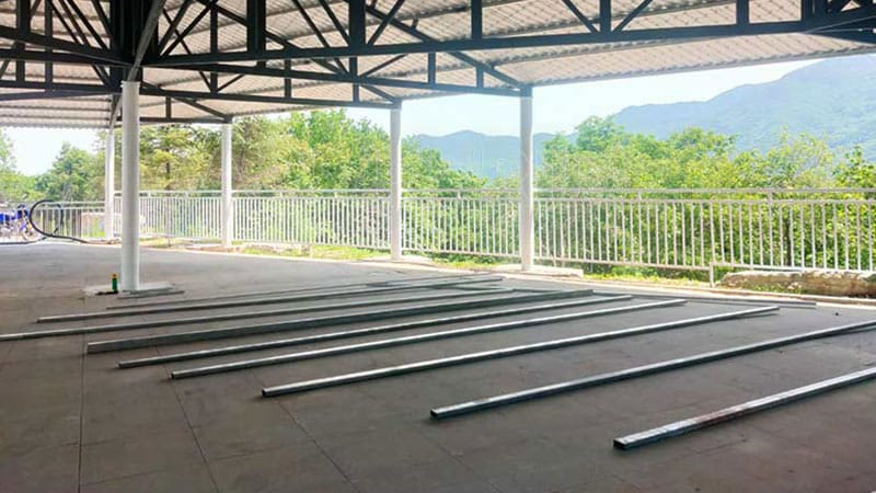 Initial stage of modular ground grid bumper car floor installation, showing steel frame rails laid under a covered structure.