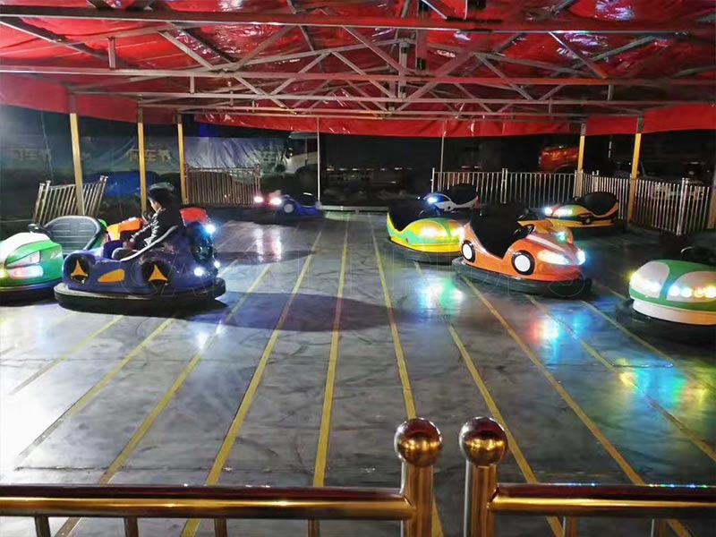 Night-time bumper car arena with LED floor lights, featuring ground grid electric bumper cars running on conductive steel tracks.