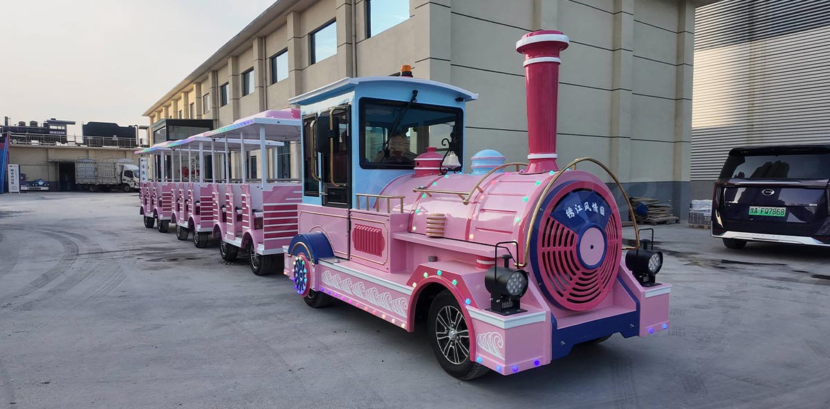 A newly manufactured pink electric trackless train undergoing outdoor driving tests at the amusement rides factory before client delivery.