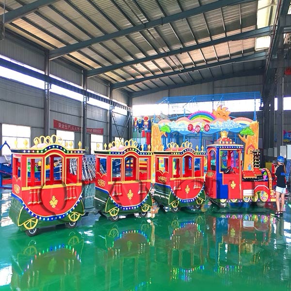 An ornate royal carriage-style electric trackless train parked inside an indoor amusement park, featuring intricate gold detailing and safe enclosed cabins.