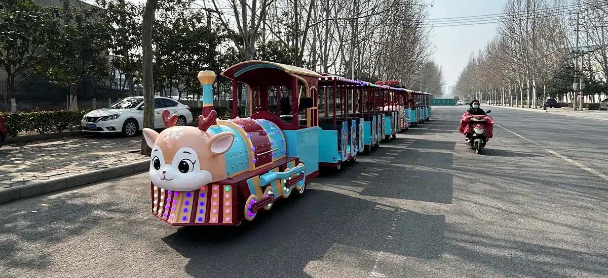 Cartoon kiddie trackless train ride operating outdoors with LED lights and multiple passenger carriages