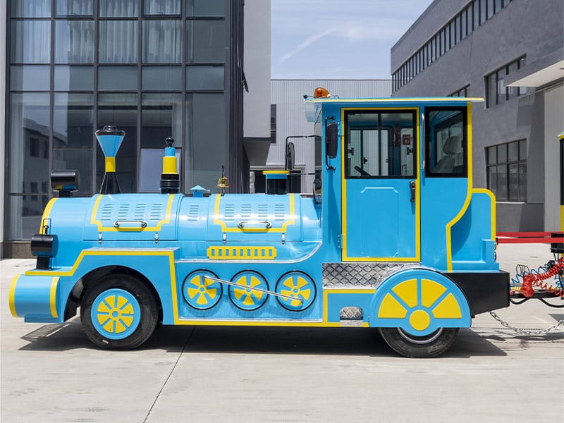 Blue electric trackless train locomotive showing the road wheels, driver cab and body structure from the side
