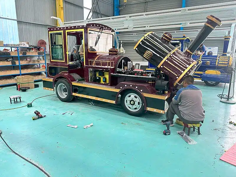 Technician assembling a commercial trackless train locomotive inside the factory workshop