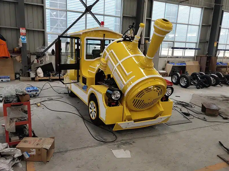 Yellow trackless train locomotive undergoing assembly and electrical preparation inside the Carnee Rides factory